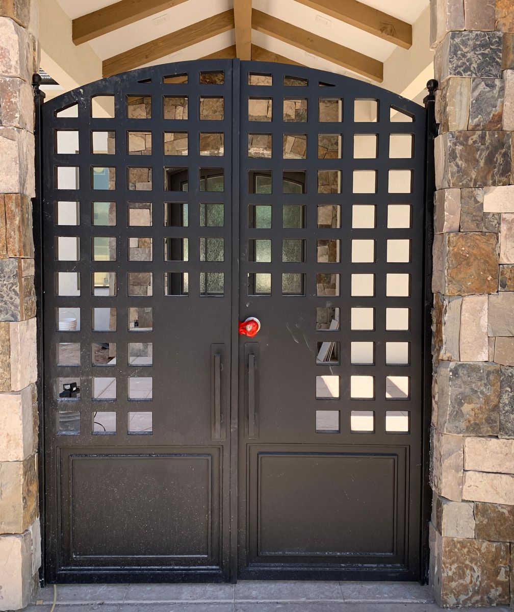Black iron double courtyard gate with square grid pattern between stone columns