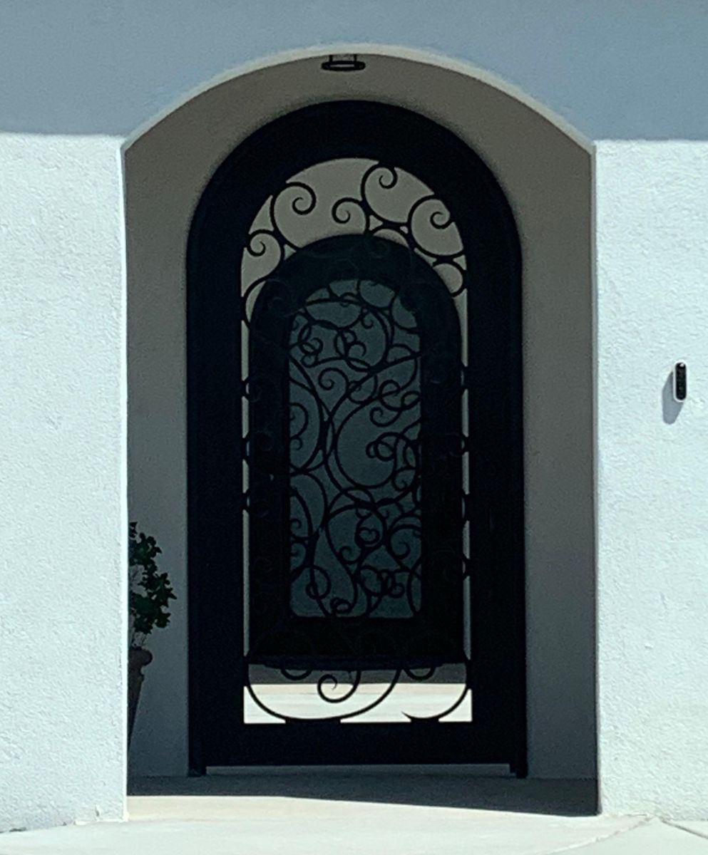 Round-top wrought iron entry door with scrollwork in a white stucco arch